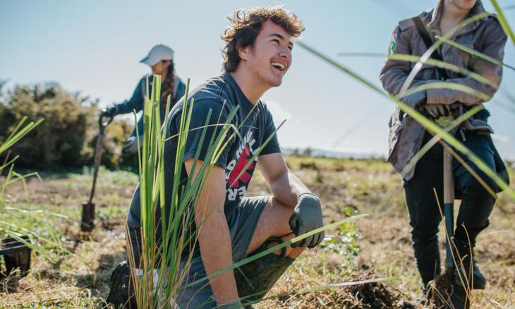 Young man smiling while planting a cabbage tree outside.