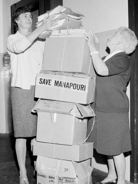Two female Forest & Bird staff help to stack a 1.5 metre tall pile of boxes containing petitions for the "Save Manapouri" campaign.