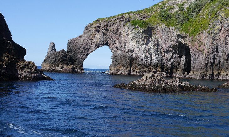A rocky outcrop into the ocean with a cathedral-like hole looking to the horizon. 