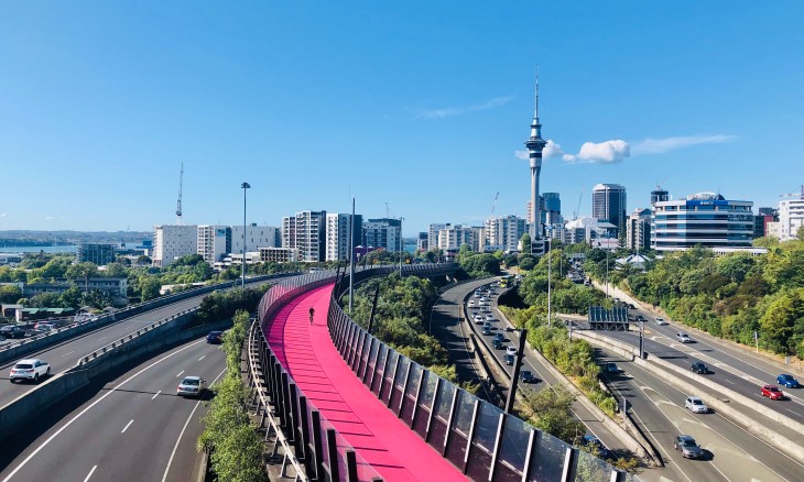 Auckland skyline with Sky Tower on a sunny day, with motorways and the bright pink cycle path in the foreground.