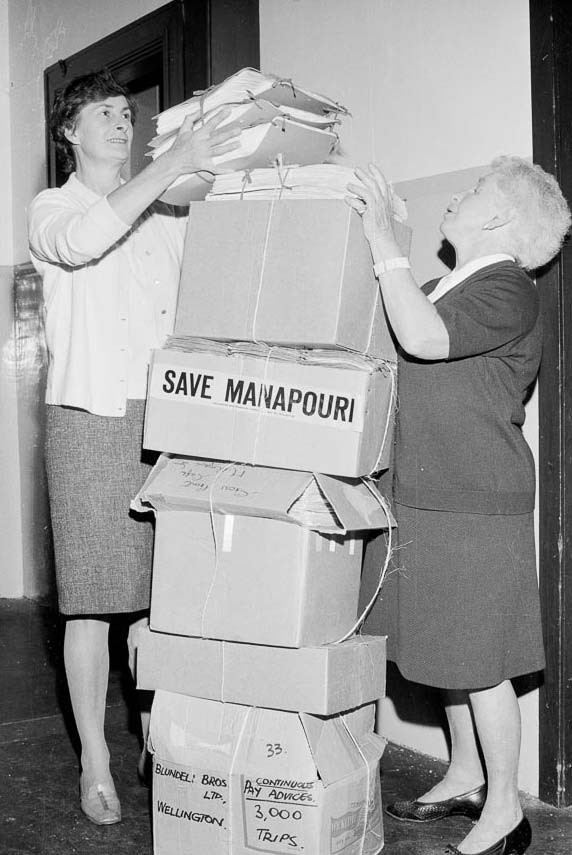 Two female Forest & Bird staff help to stack a 1.5 metre tall pile of boxes containing petitions for the "Save Manapouri" campaign.